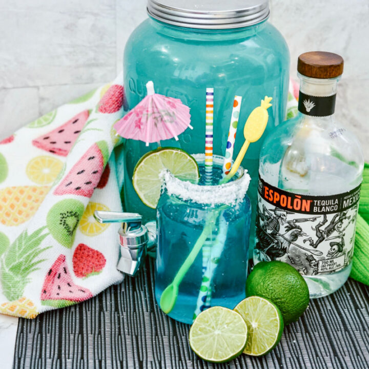 pitcher of blue margaritas on a table with ingredients